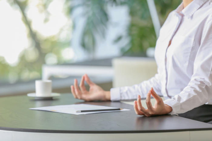 Female employee sitting at desk meditating with fingers and thumbs making circle