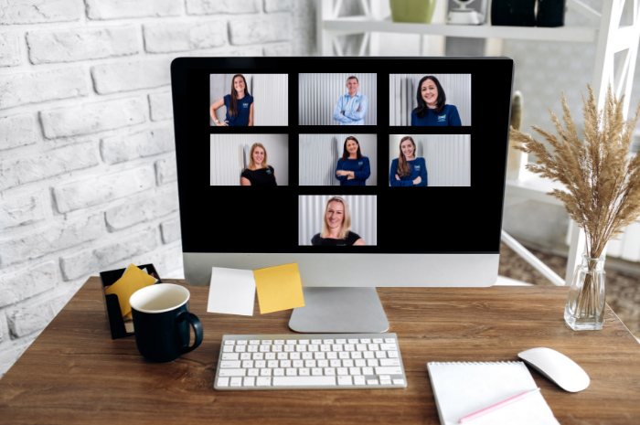 Computer screen showing team members on zoom with stationery and coffee on desk