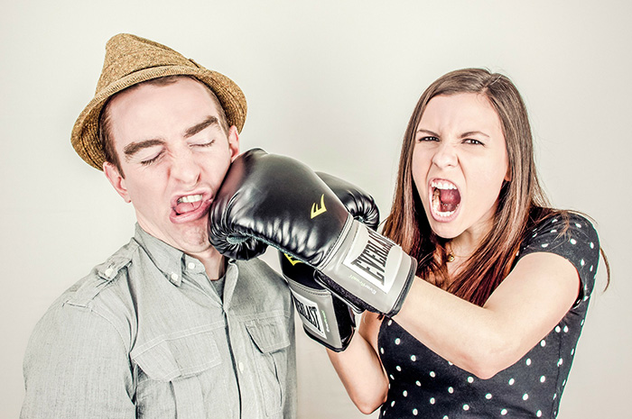 Female with boxing gloves on punching male wearing a hat on the cheek side of face