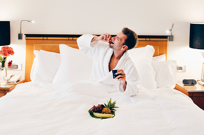 Man in bath robe sitting in bed with white linen eating fruit platter