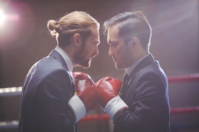 Two men in business suits wearing red boxing gloves in attack mode with fists up
