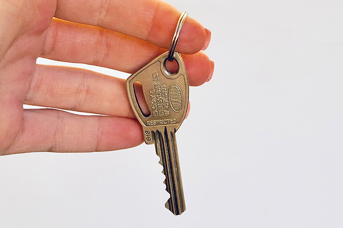 Hand holding single key in front of white background