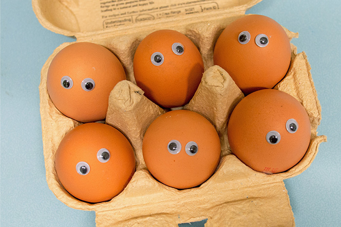 Six eggs in egg carton with stick on eyes placed on each