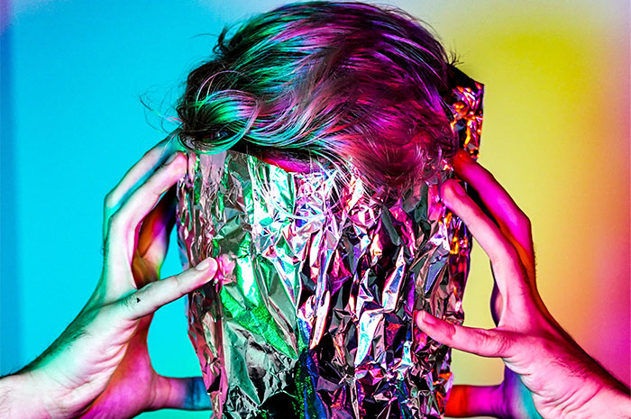 Man with foil over his face holding his head in front of colourful backgroun