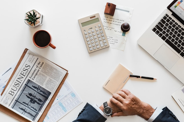 Desk with Business newspaper laptop calculator stationery and coffee man looking at watch