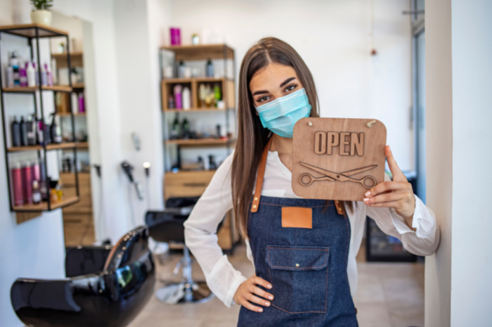 Hairdresser wearing hygiene mask holding up OPEN sign