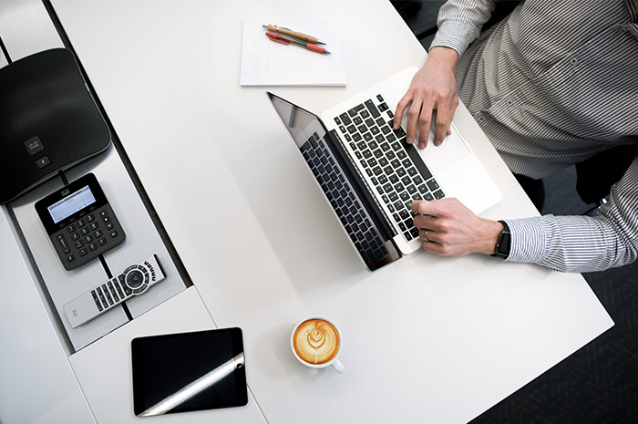 Man working at laptop on desk with coffee stationery calculator printer and remote control