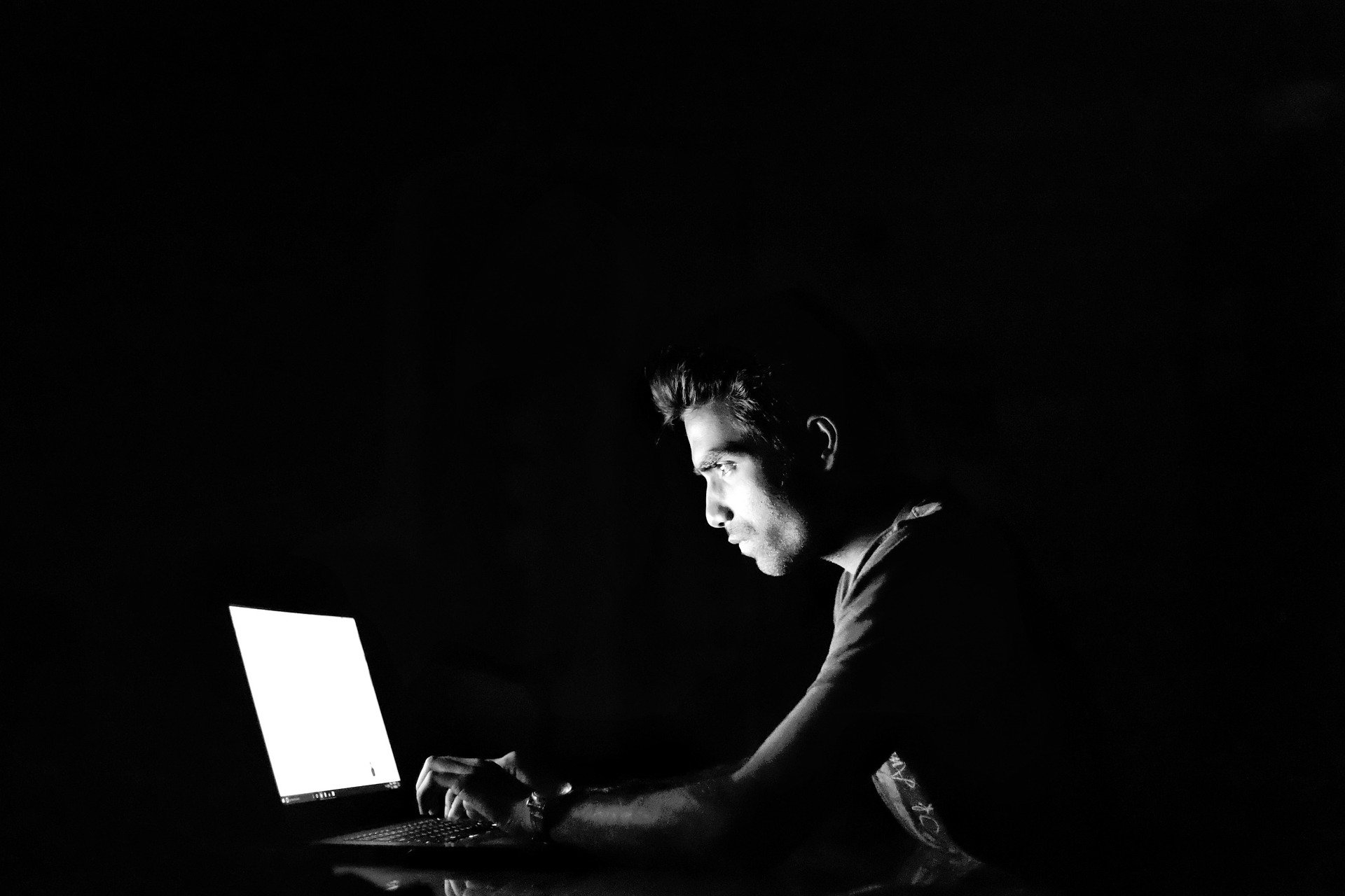 Man sitting in the dark on laptop typing