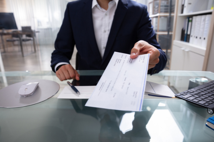 Man in business attire sitting at desk holding out cheque for collection