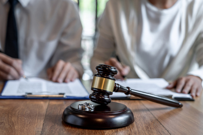 Husband and wife sitting at desk in front of divorce papers gavel and wedding rings