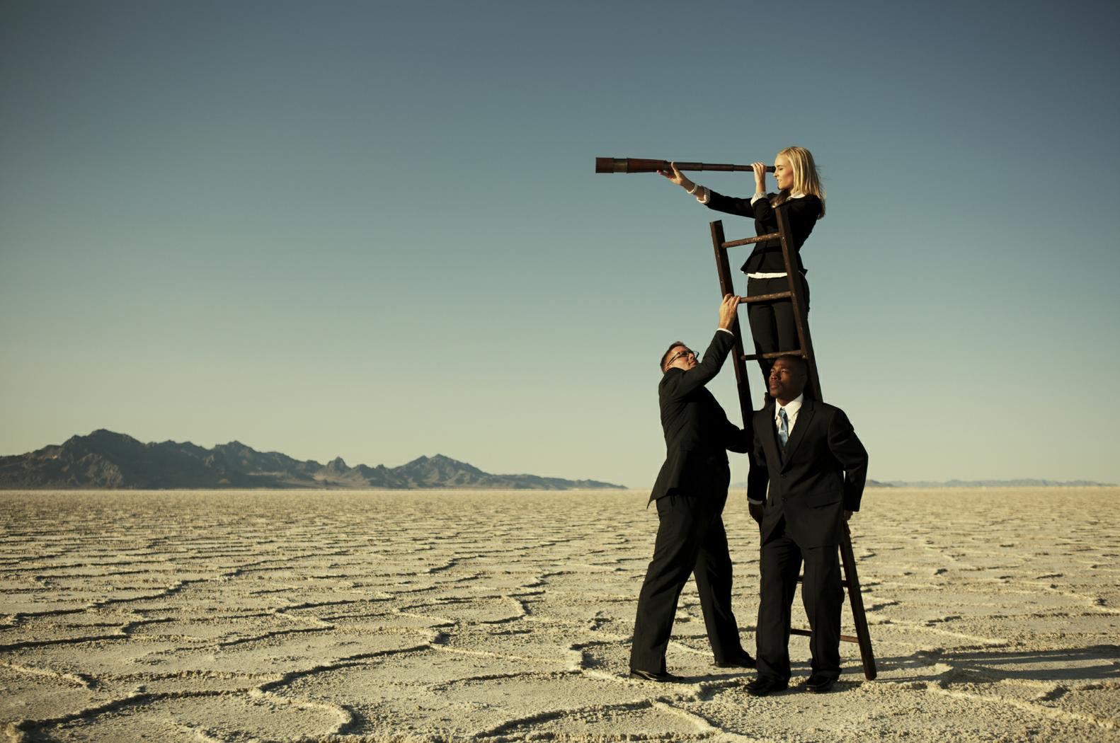 Two men in black business suits holding up a ladder with a business woman peering into a telescope at the top of the ladder