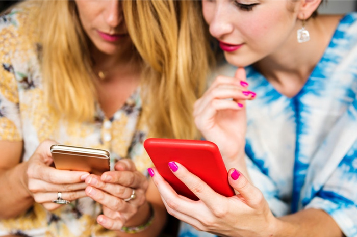 Two women looking at phones in colourful dresses