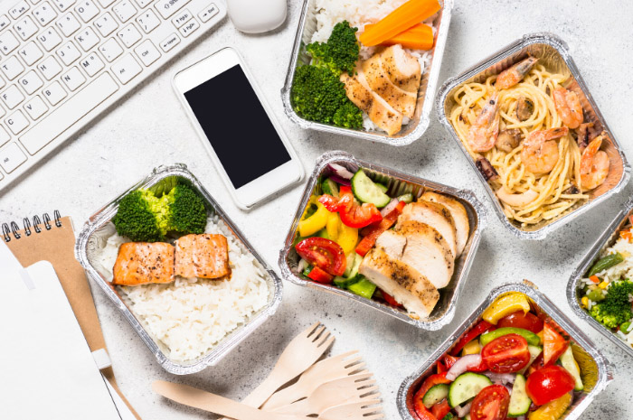 A variety on healthy food dishes on desk near computer keyboard and phone