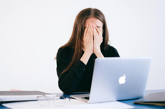 Woman sitting at desk in front of computer with head in her hands stressed