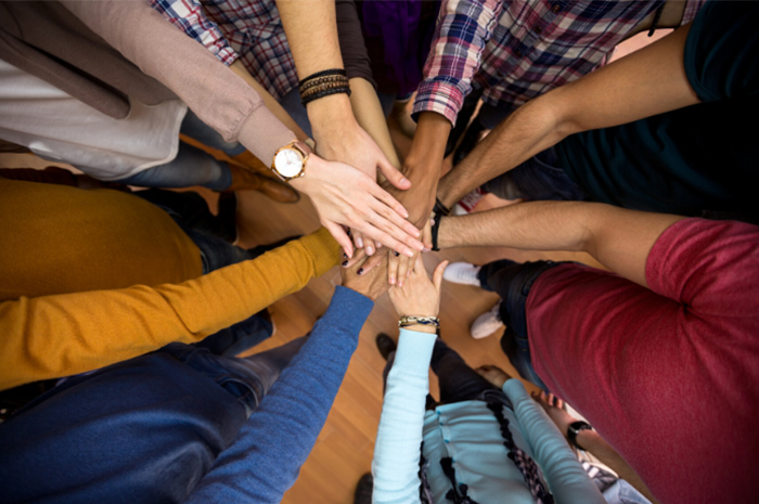 Hands of different skin types in middle of circle ready to team huddle