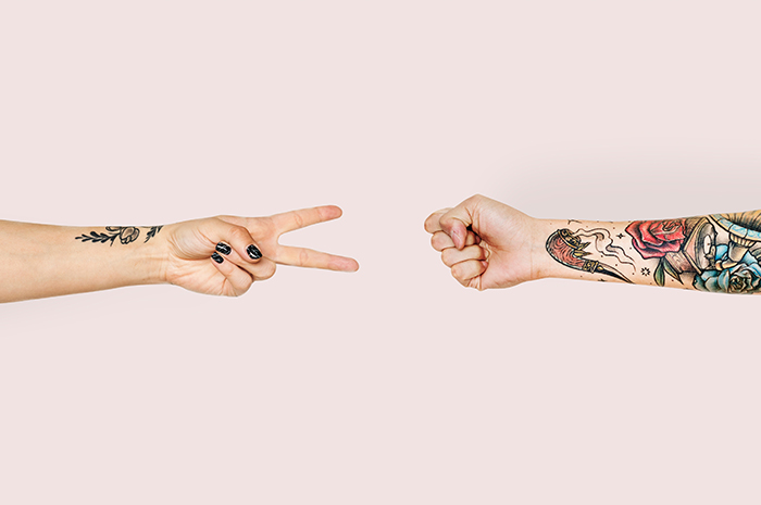 Two arms with tattoos playing paper scissors rock