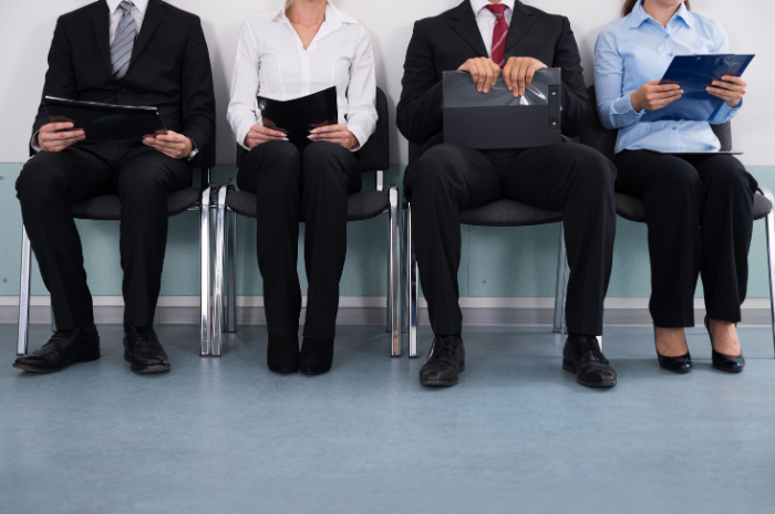 People dressed in corporate attire sitting in waiting room holding CV documentation for interview