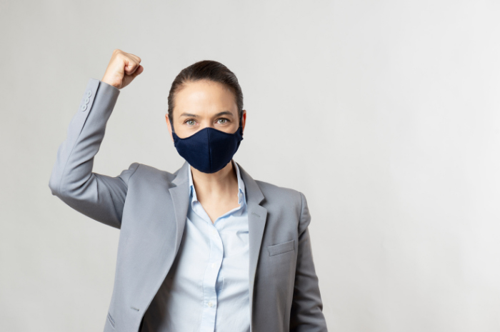 Female employee wearing mask cheering with one arm up and hand in a fist