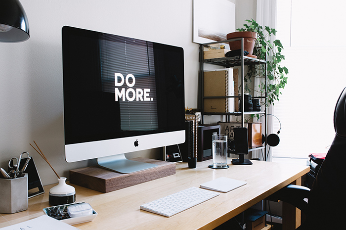 Desk with Mac computer and stationery plant with wording on screen DO MORE