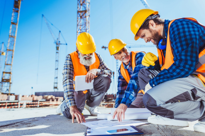 Tradesmen on concrete slab of construction site pointing to documents