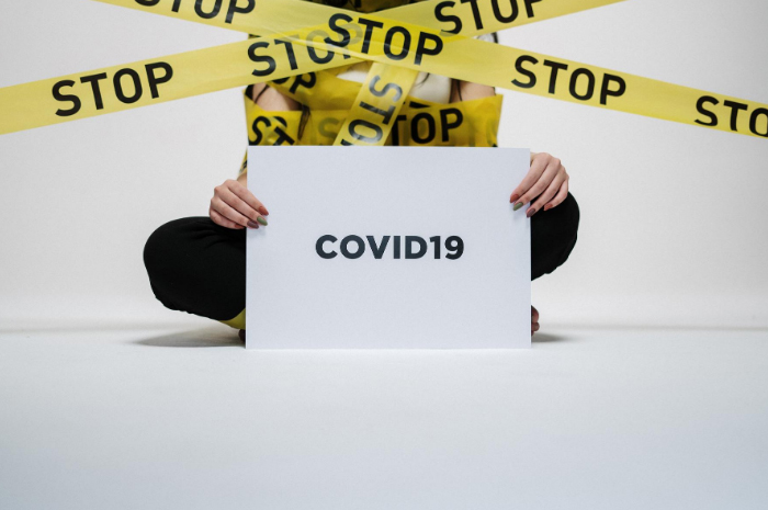 Sign saying COVID19 held up by person wrapped in yellow tape with STOP wording