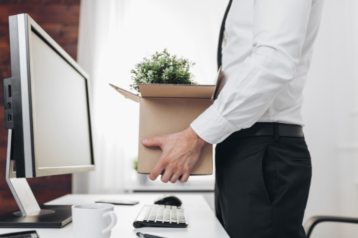 Male employee standing at desk holding a moving box full of office contents upon termination