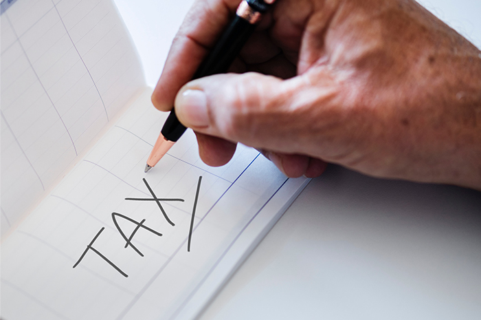 Man holding pen writing word TAX on paper