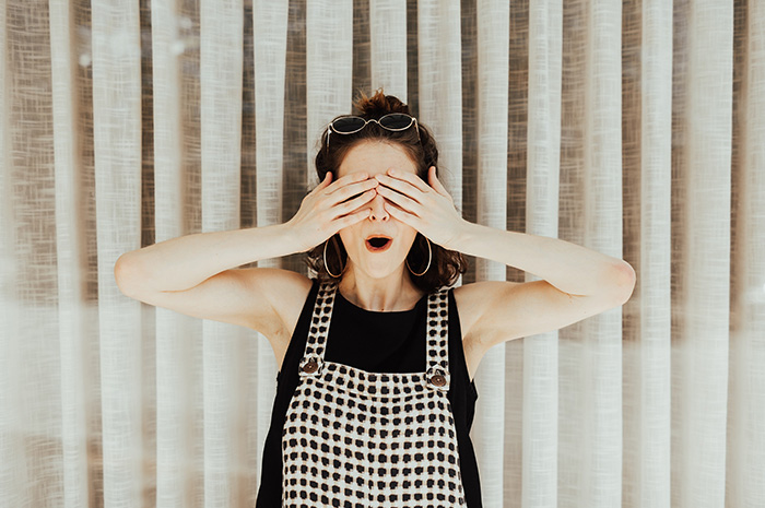 Woman holding hands over eyes cheering standing front of curtain