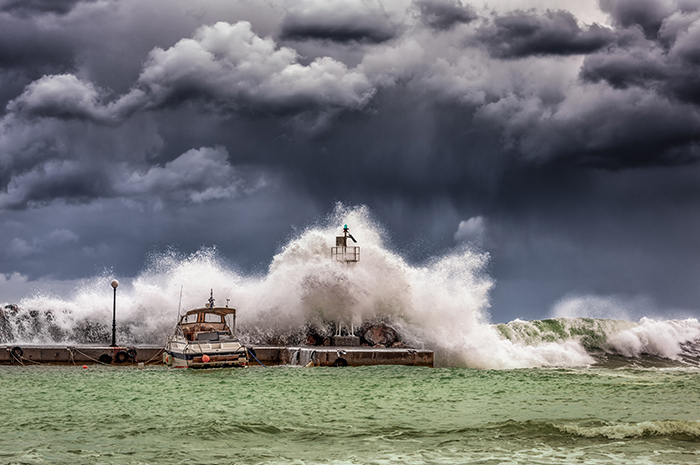 Tsunami of water over pier crashing into boat with grey angry skies