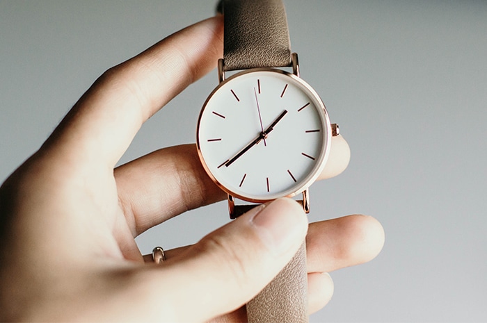 Hand holding watch with white face gold hardware and beige band