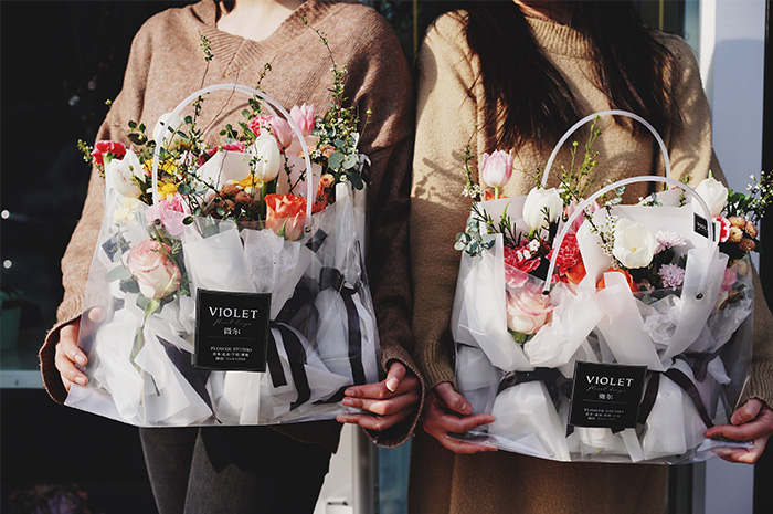 Two women holding large clear bags of wrapped flower bunches