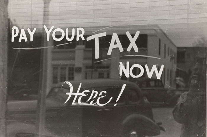 Old sign on glass window in olden days saying PAY YOUR TAX NOW HERE!