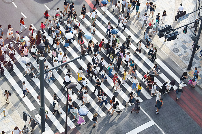 Crowd of people walking across wide pedestrian crossing past traffic lights