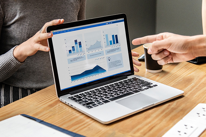 Laptop on desk with charts and graphs and hands of two people pointing to screen