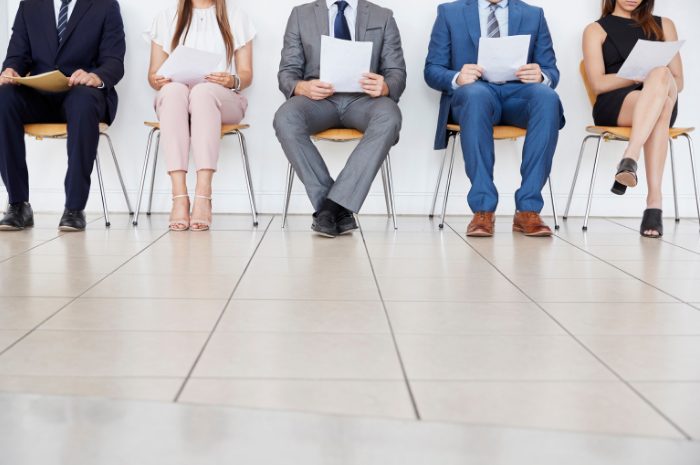 Row of seated people in corporate attire in interview waiting room