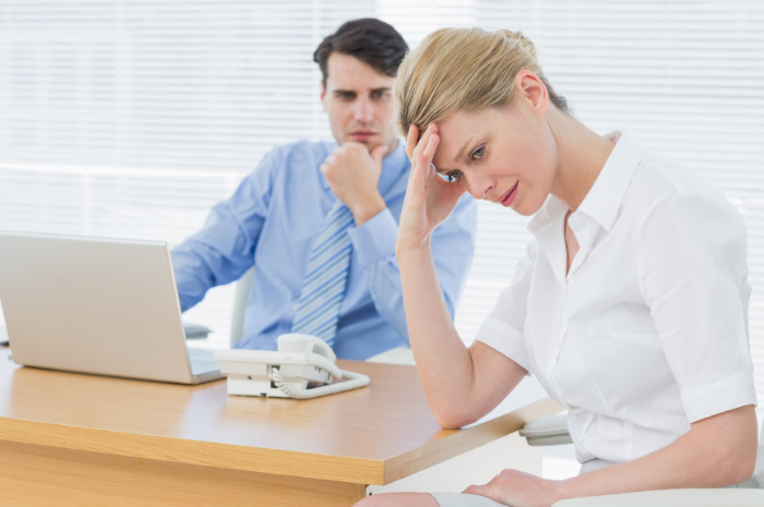 Female employee placing hand on forehead with male employee cross in the background