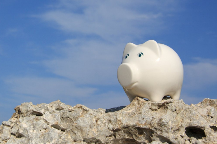 White piggy bank standing on rock with blue sky and clouds in the background