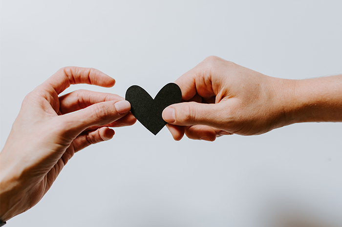 Hand passing black heart cut out to other hand