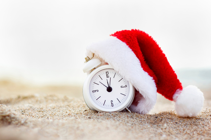 Alarm clock wearing a Santa hat resting on the sand