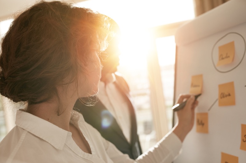 Woman writing on white board with sticky notes attached