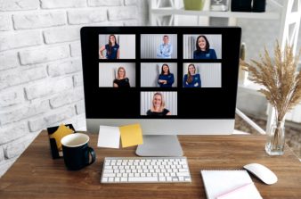 Computer screen showing team members on zoom with stationery and coffee on desk