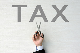 Man in corporate attire holding scissors up to word TAX