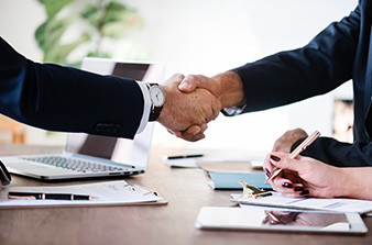 Business men shaking hands over desk with laptop and documentation