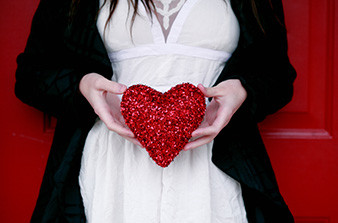 Female wearing white shirt and black jacket holding red sparkly love heart