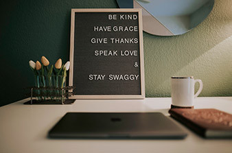 Sign with inspirational wording on table with closed laptop cup of coffee book and flowers