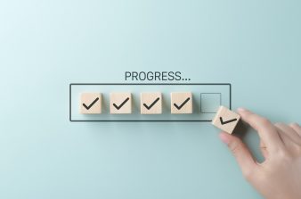 A hand placing the final checkmark on wooden blocks in a progress bar
