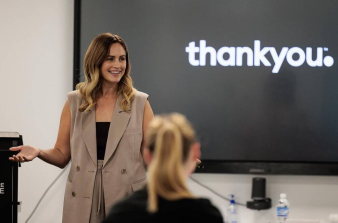 Female presenter standing in front of audience with a screen behind her that says "Thank you".